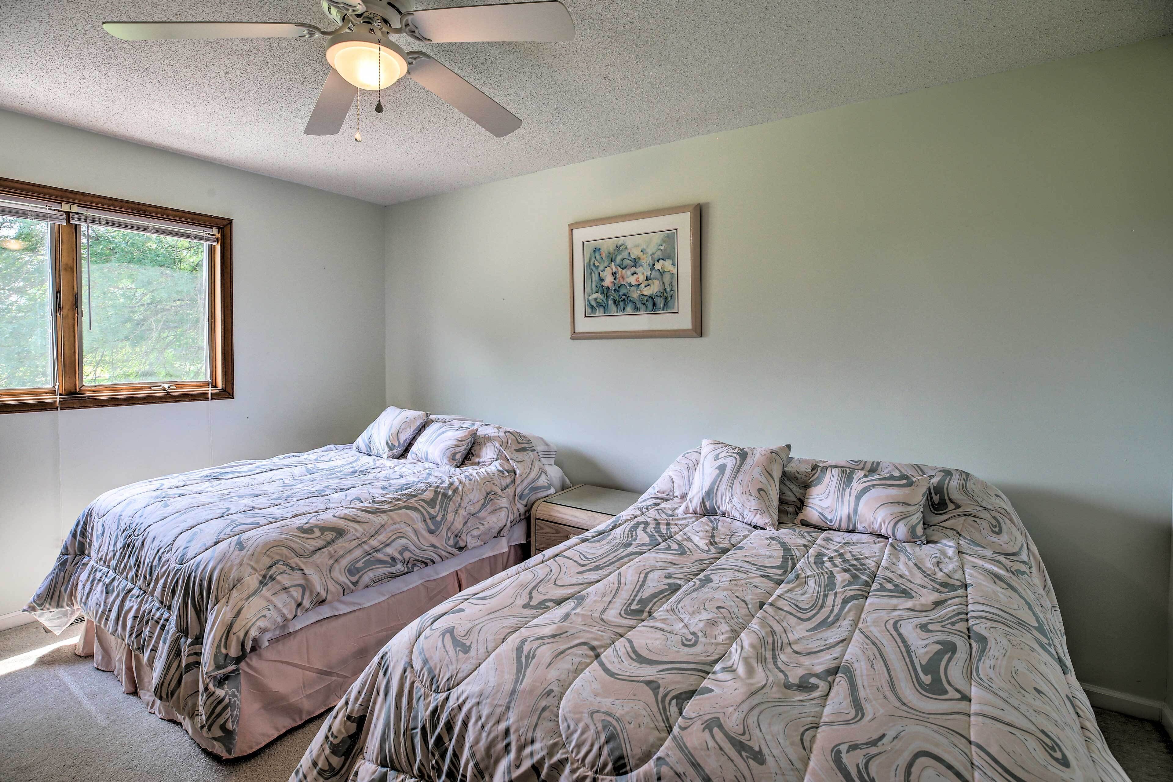 A bedroom with two beds, a ceiling fan, a window, and a framed picture on the wall.
