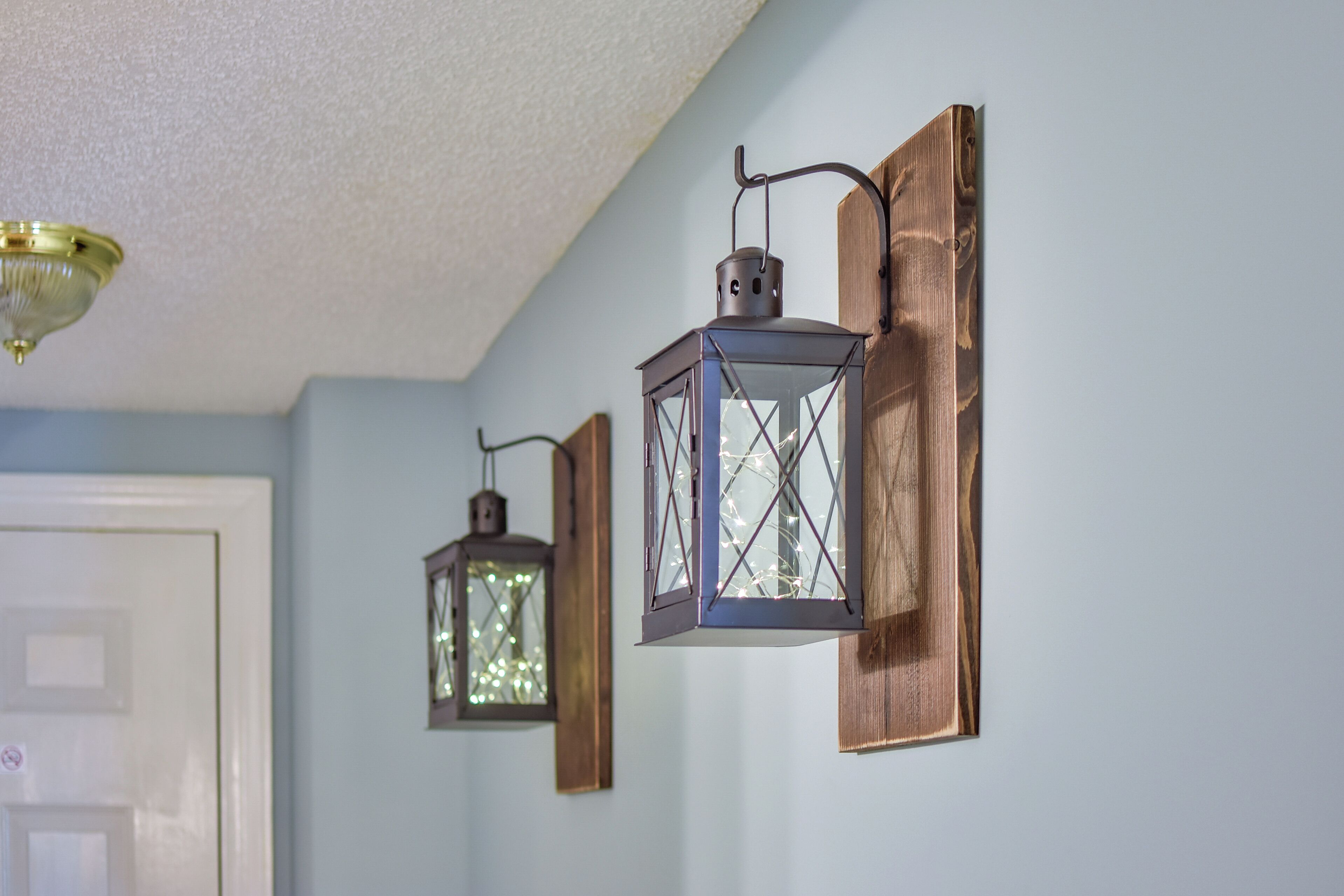 Two wall-mounted lanterns with a rustic design, a ceiling light fixture, and a door in the background.