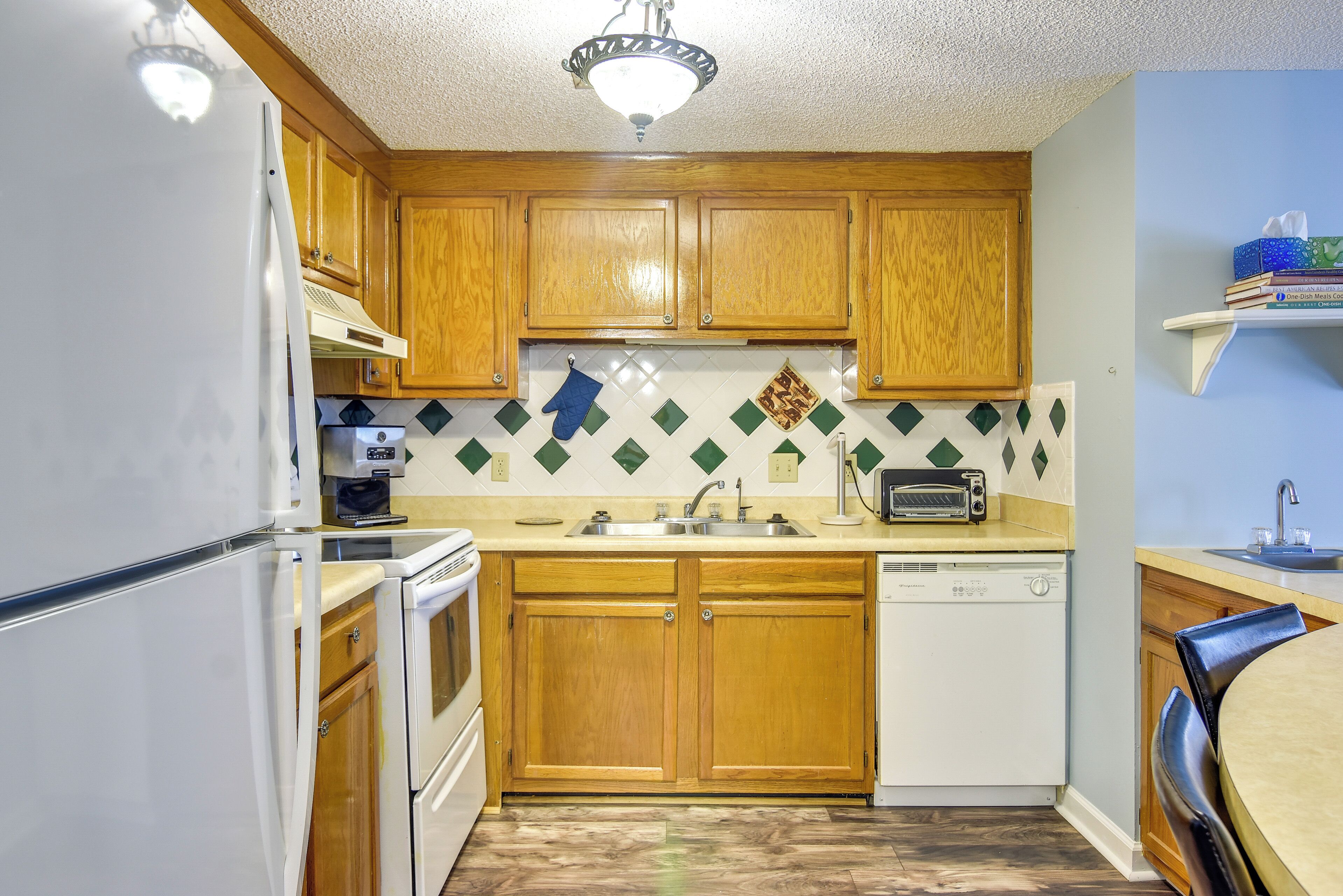 A compact kitchen with wooden cabinets, a white refrigerator, a dishwasher, and a microwave.