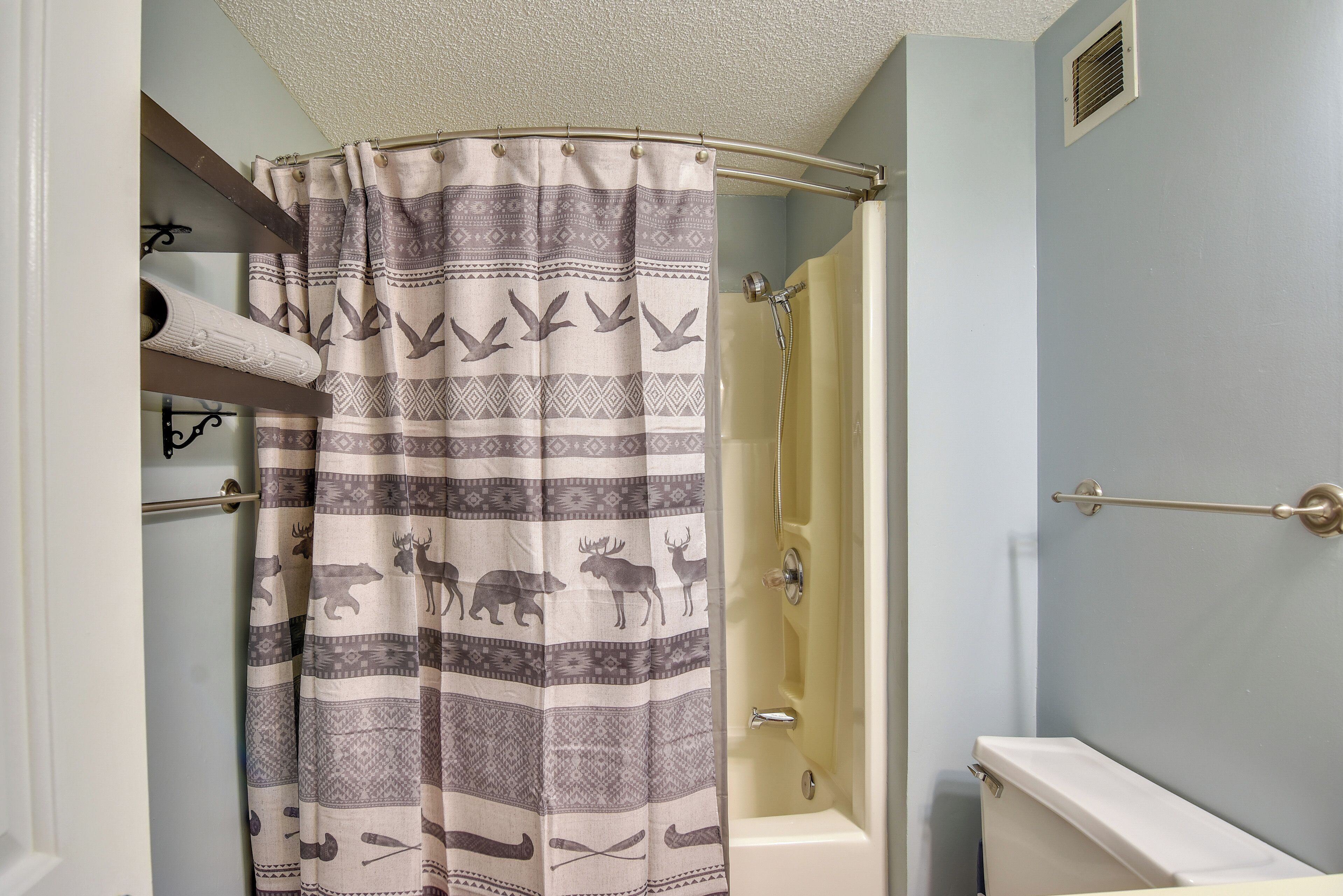 Un baño con cortina de ducha estampada con animales, una bañera y un perchero para toallas.