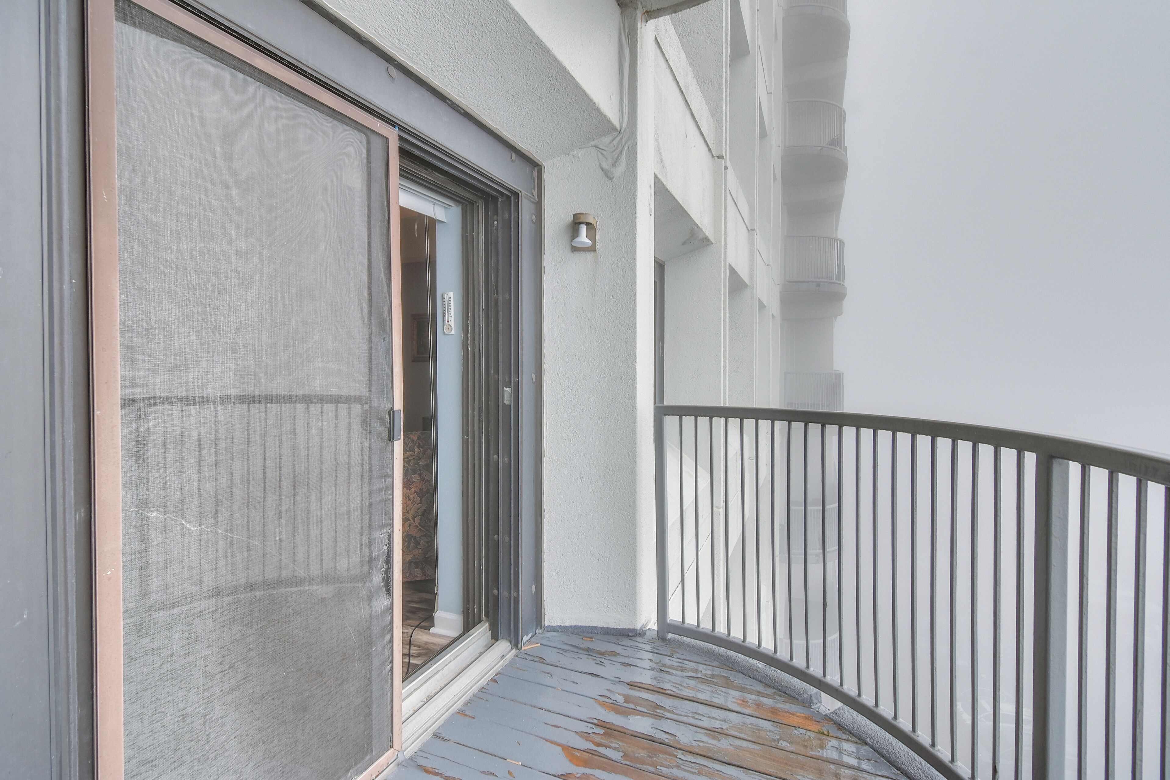 Een balkon met een metalen hekwerk, een schuifdeur en een klein, aan de muur bevestigd lampje.
