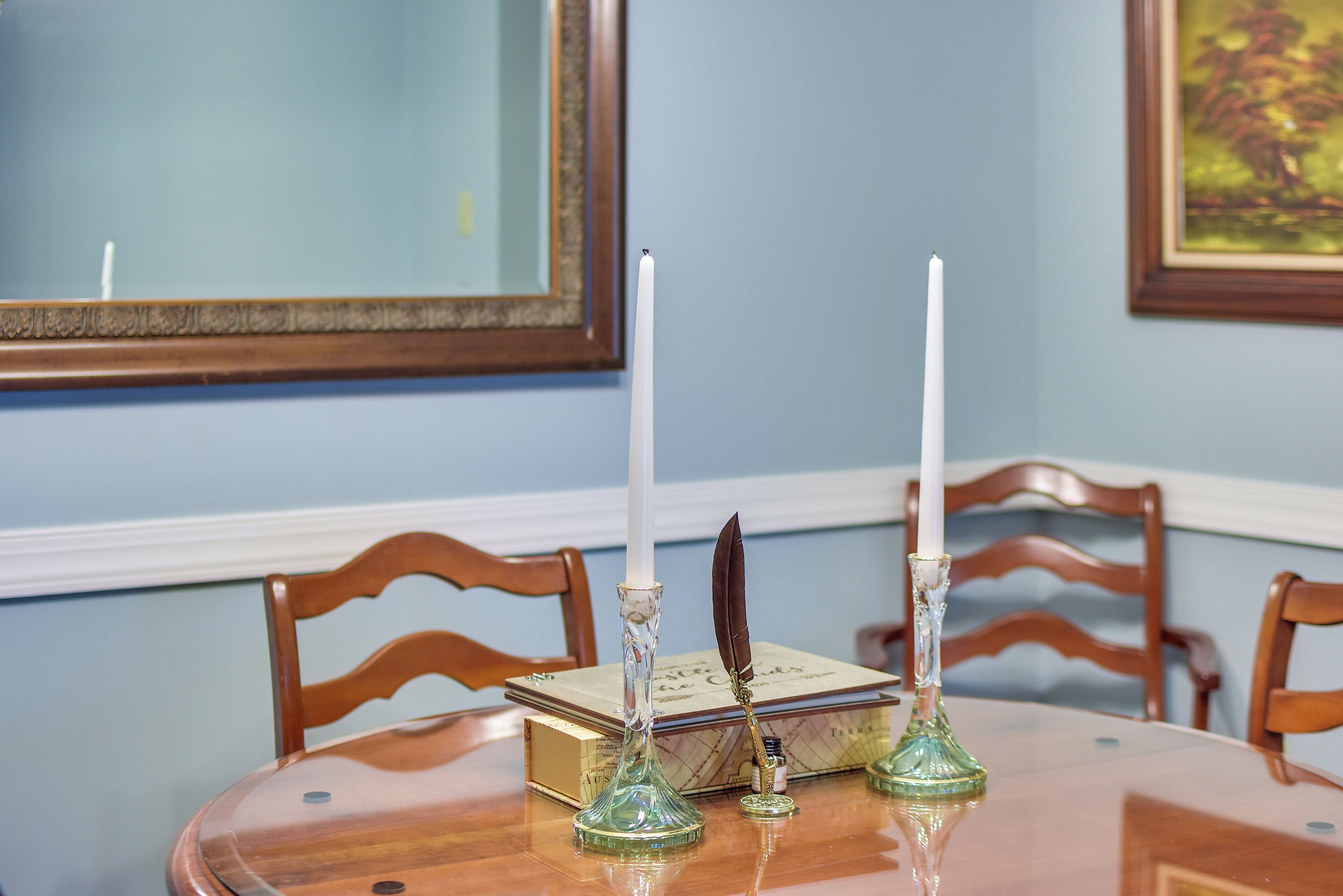 A dining table with two candlesticks, a book, and a quill pen.