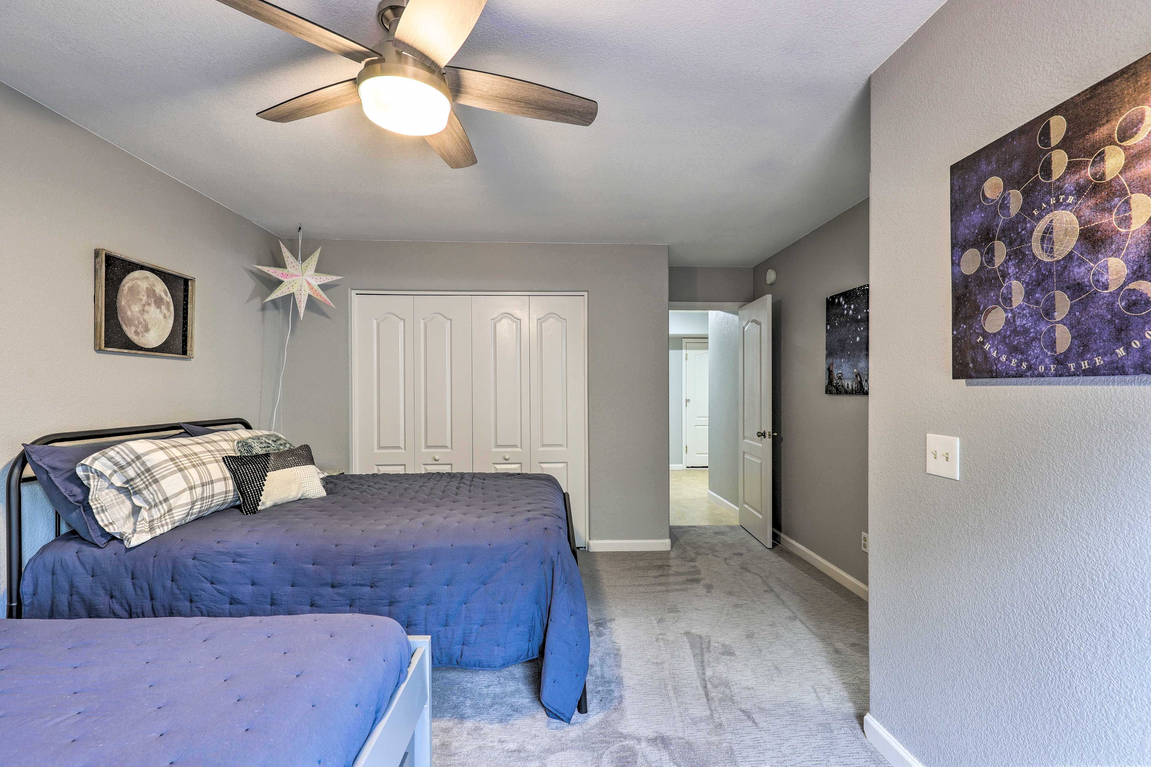 A bedroom with a bed, a ceiling fan, a star decoration, a framed picture of the moon, and a wall art depicting the moon's phases.