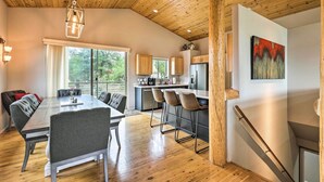 A modern kitchen with wooden cabinets and a central island, a dining area with a long table and chairs, and a staircase with a wooden railing.