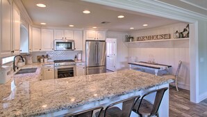A kitchen with white cabinetry, a granite countertop, stainless steel appliances, and a 'FARMHOUSE' sign.
