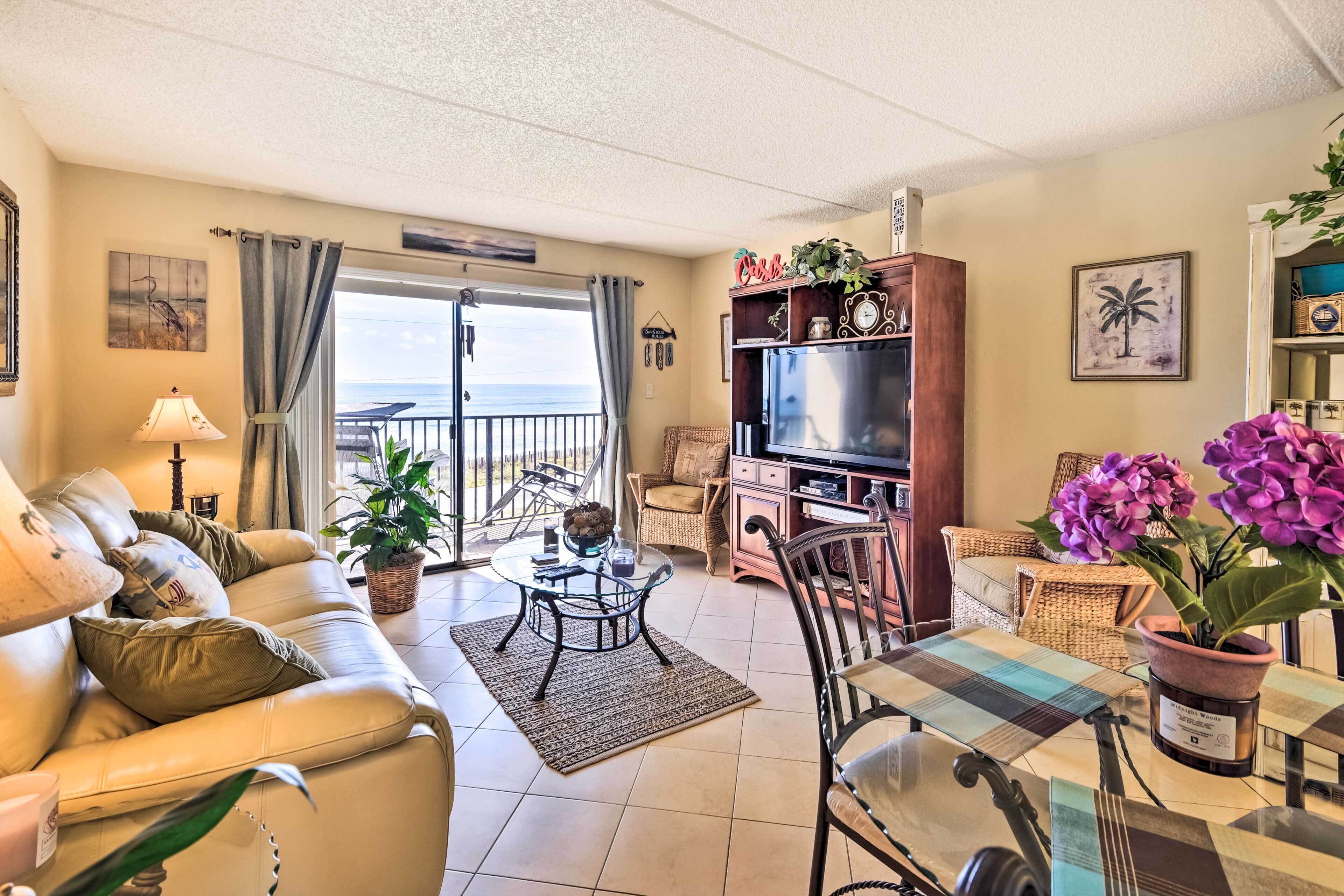 A living room with a sofa, a coffee table, a TV stand, and a balcony with a view of the sea.
