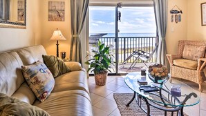 A living room with a leather sofa, a wicker chair, a glass coffee table, and a view of the sea through a sliding glass door. - Ormond Beach Condo w/ Balcony & Views (Ormond Beach)