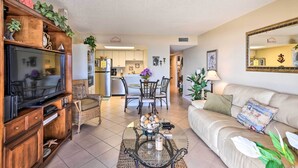 A living room with a television, sofa, and coffee table. There is a dining area with chairs and a table in the background. - Ormond Beach Condo w/ Balcony & Views (Ormond Beach)