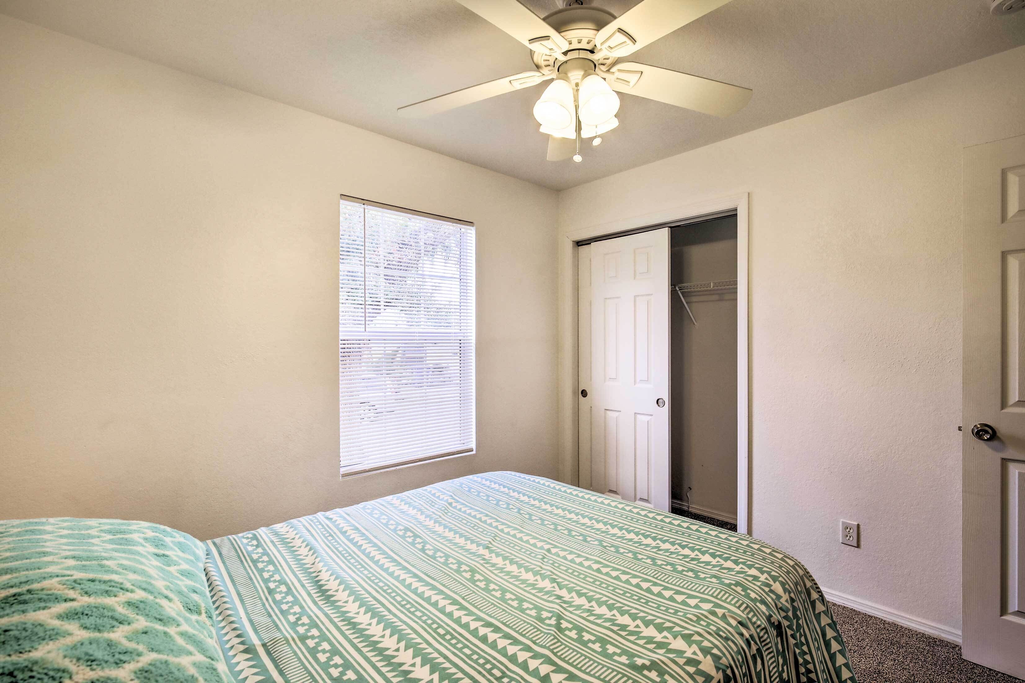 A bedroom with a bed, a ceiling fan, a window with blinds, and a door.