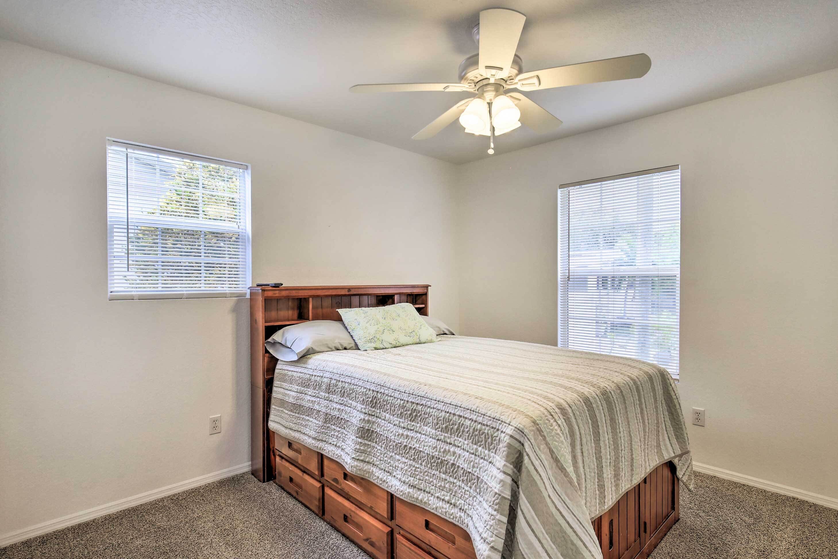 A bedroom with a wooden bed, a ceiling fan, and two windows with blinds.