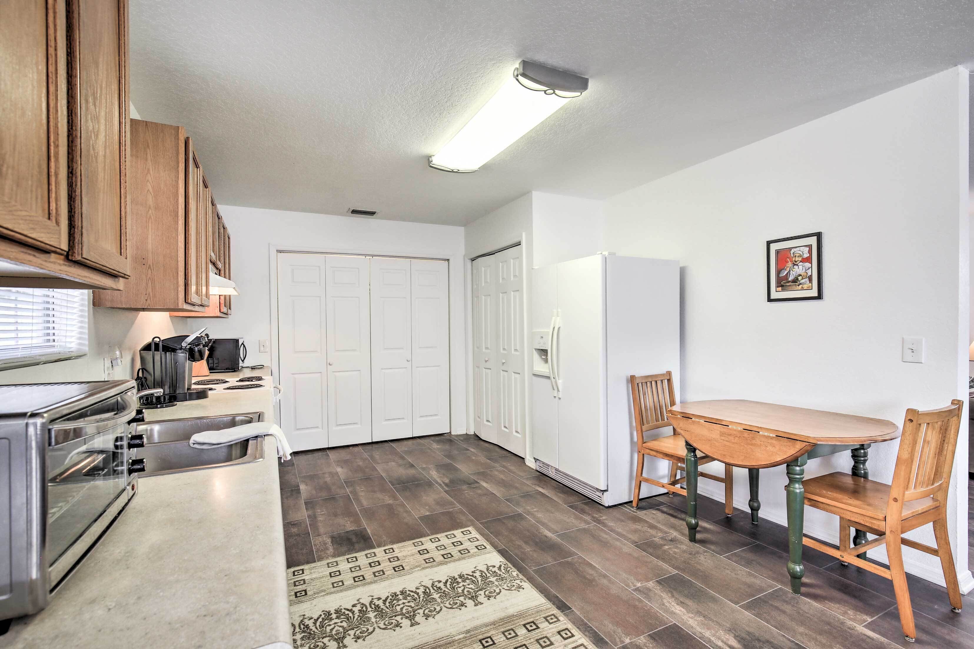 A compact kitchen with a stove, oven, and microwave. There is a dining table with chairs and a rug on the floor.