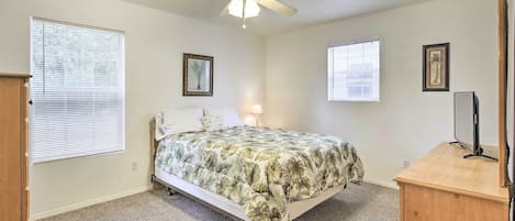 A bedroom with a bed, a ceiling fan, a desk, and two windows with blinds.