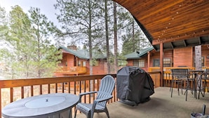 A covered outdoor deck with a table and chairs, a grill, and a view of a cabin in the background. - Pinetop Escape: Charming Mountain Condo w/ Balcony (Pinetop)