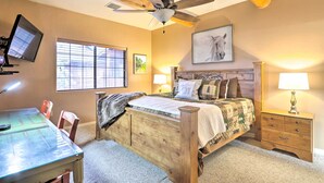 A bedroom with a wooden bed, a desk, and a chair. There is a ceiling fan, a window with blinds, and a wall-mounted TV. - Pinetop Escape: Charming Mountain Condo w/ Balcony (Pinetop)