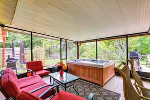 Een overdekt terrasgedeelte met een jacuzzi, rode stoelen, een glazen tafel en uitzicht op de omgeving.