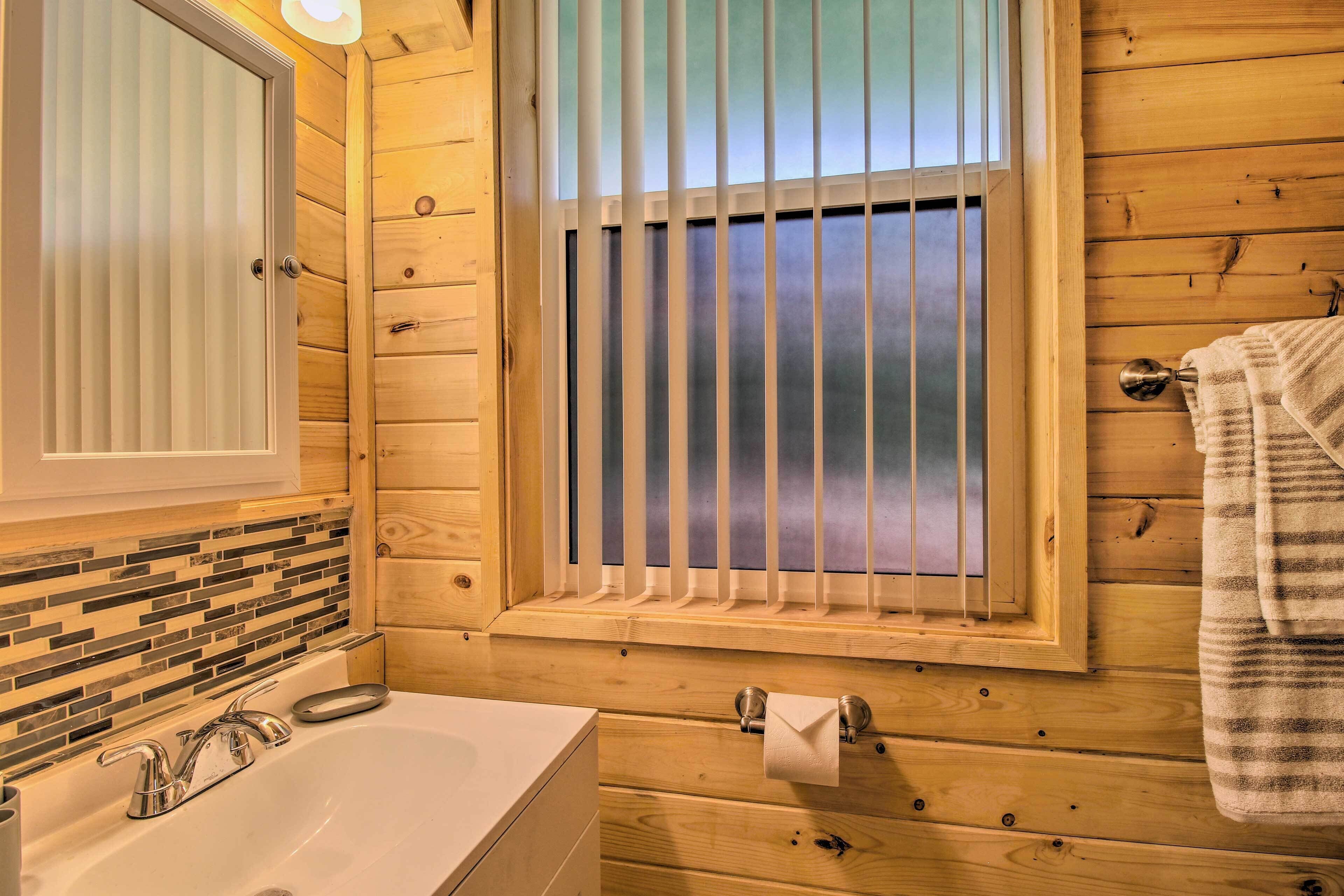 A wooden cabin bathroom with a large window, a sink with a mirror, and a towel hanging on the wall.
