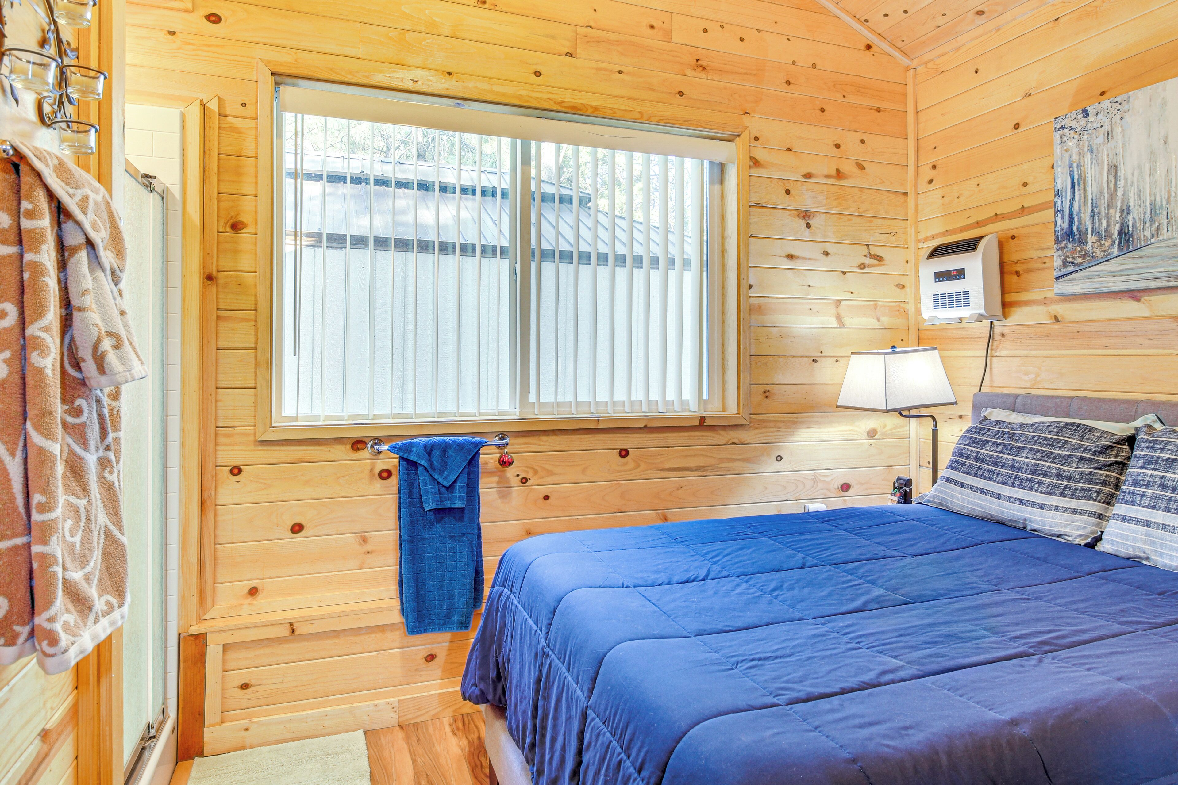 Una camera in legno con un letto, una finestra con persiane, un asciugamano appeso al muro e una lampada.