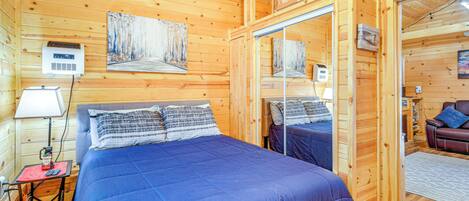 A wooden cabin room with a bed, a nightstand, a lamp, and a painting on the wall.