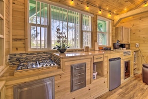 A wooden cabin kitchen with a gas stove, refrigerator, and a window with a view of trees.