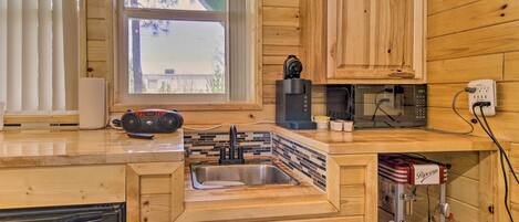 A compact kitchen with wooden cabinetry, a built-in sink, a coffee maker, a microwave, and a dishwashing unit.