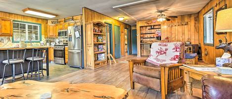 A rustic interior with wooden walls, a kitchen area, a dining space with a table and chairs, and a leather sofa.