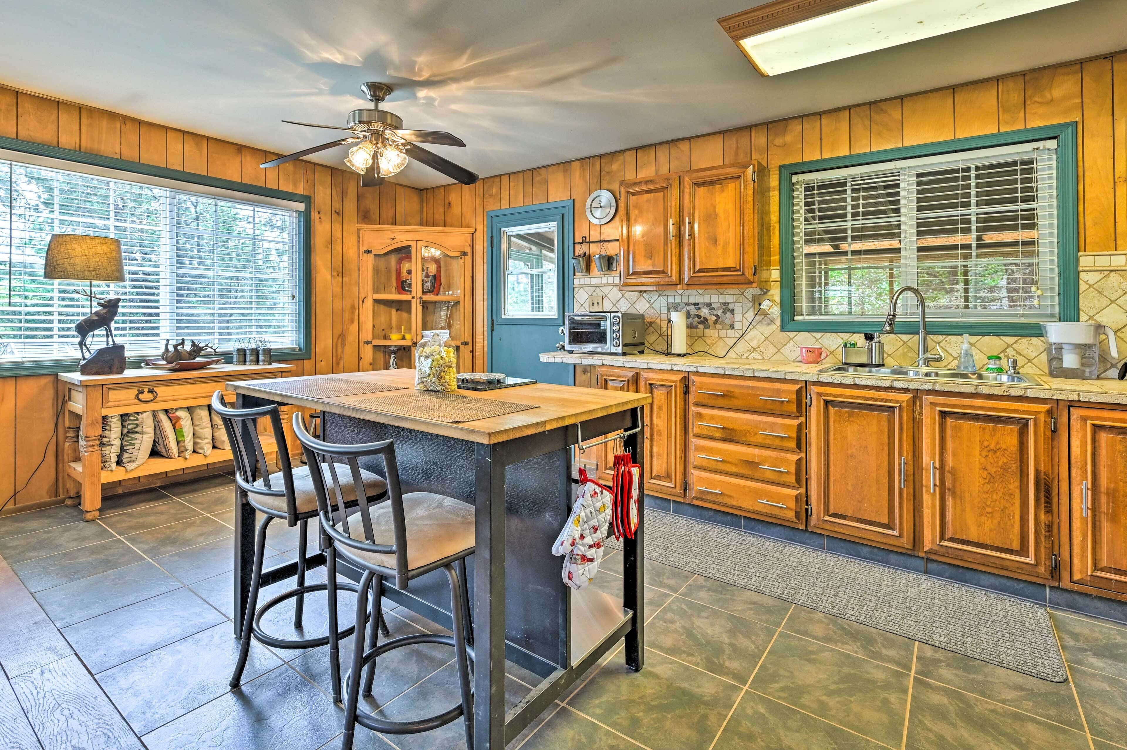 A kitchen with wooden cabinets, a bar stool area, a built-in oven, and a large window with blinds.