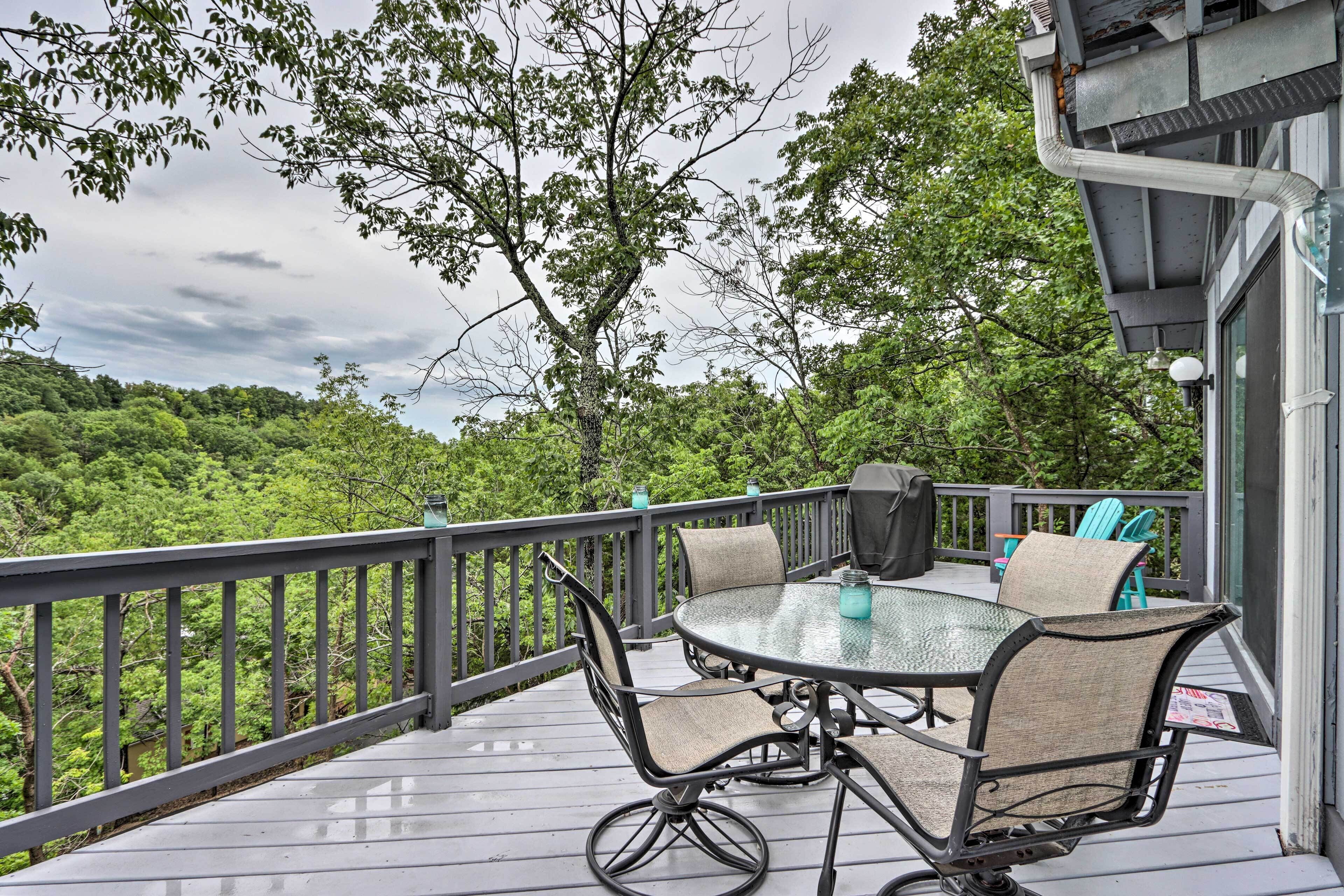 A covered outdoor deck with a glass-top table and chairs, surrounded by a metal railing.