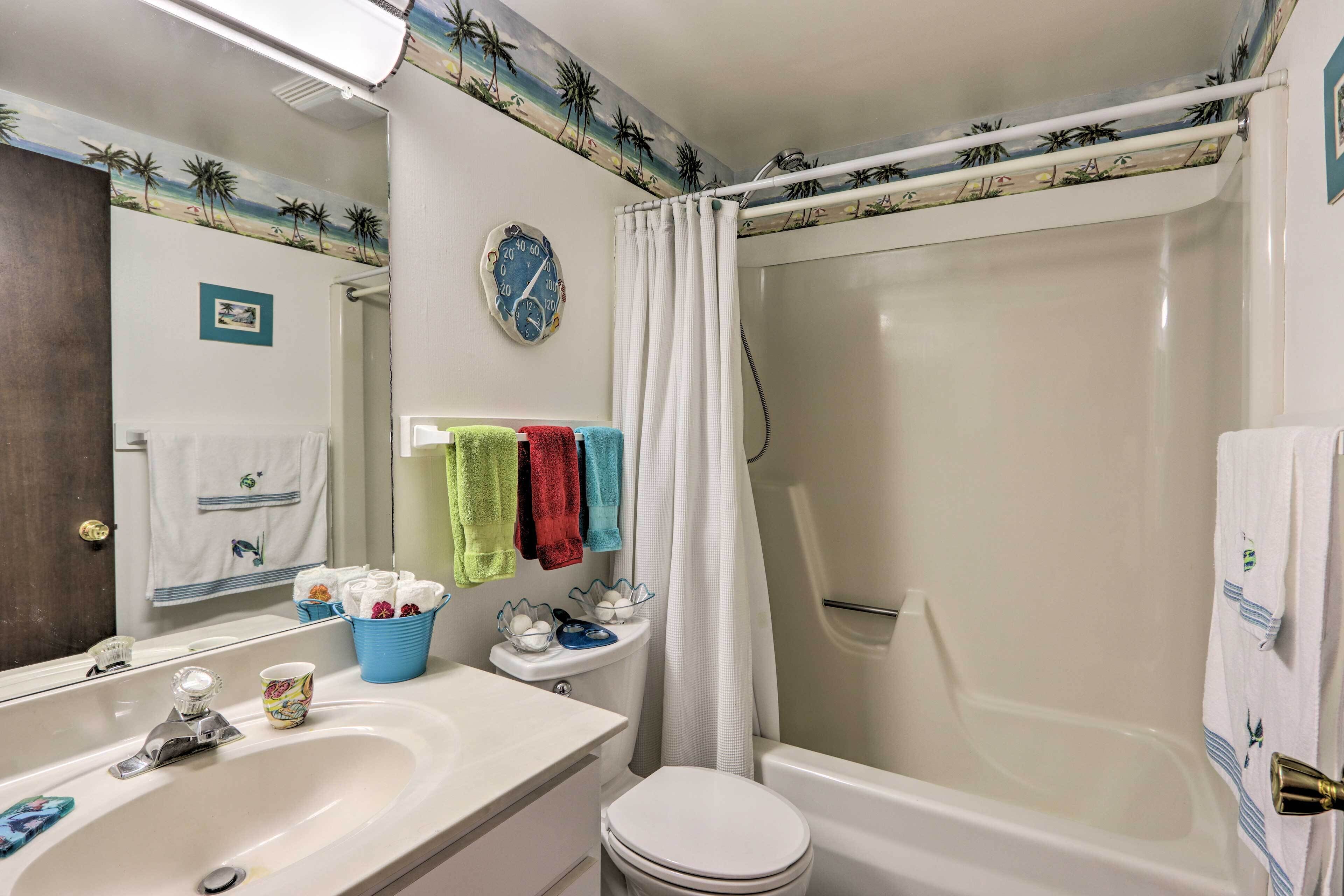 A bathroom with a white sink, a toilet, a bathtub, and a shower curtain. There is a clock on the wall and a small picture frame.
