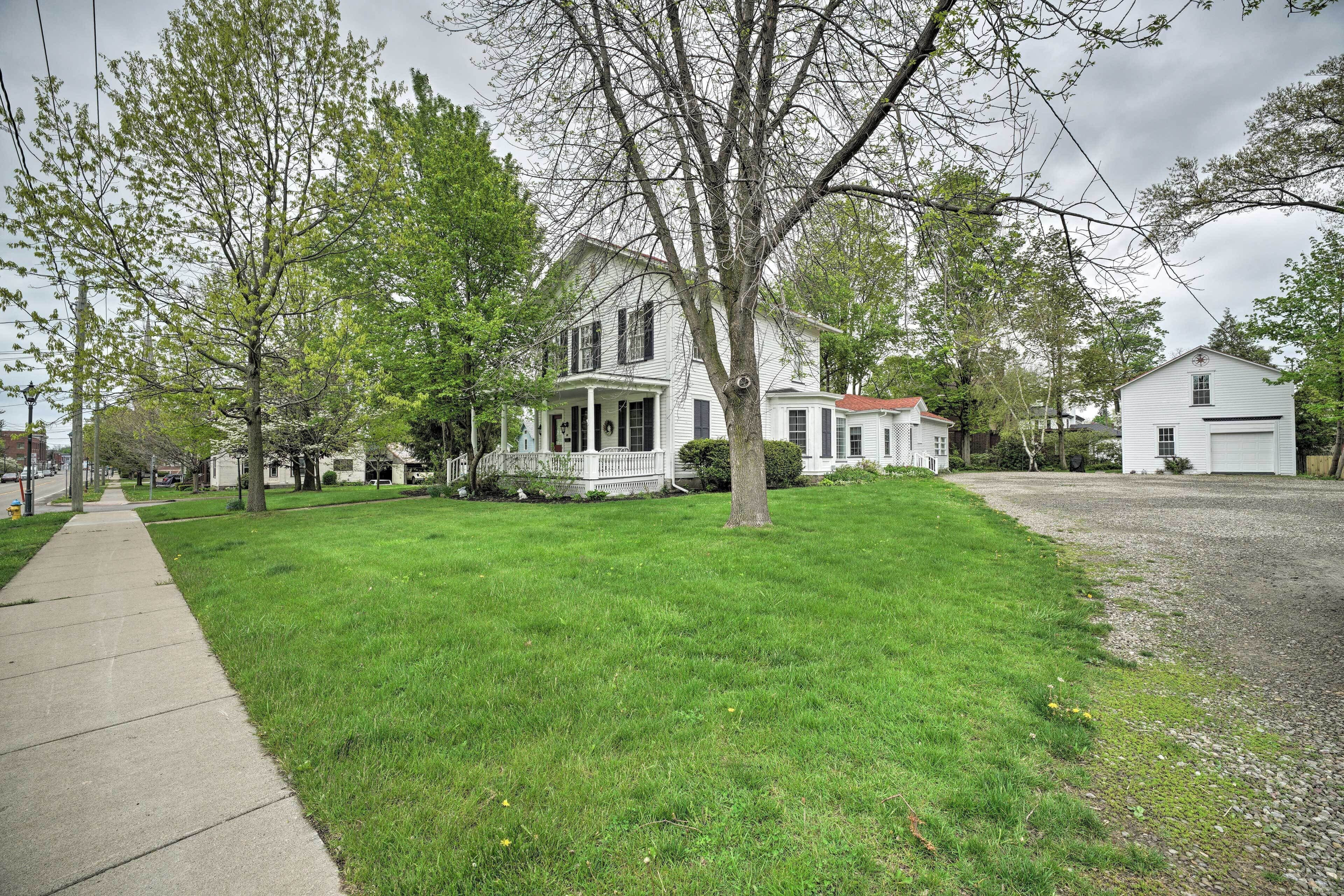 A residential area with a large white house, a well-maintained lawn, and a sidewalk.