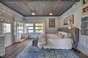 Un dormitorio con una cama grande, techo de madera, alfombra azul estampada y un cartel que enumera ciudades.