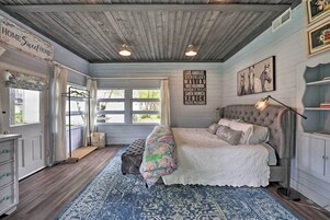 Un dormitorio con una cama grande, techo de madera, alfombra azul estampada y un cartel que enumera ciudades.