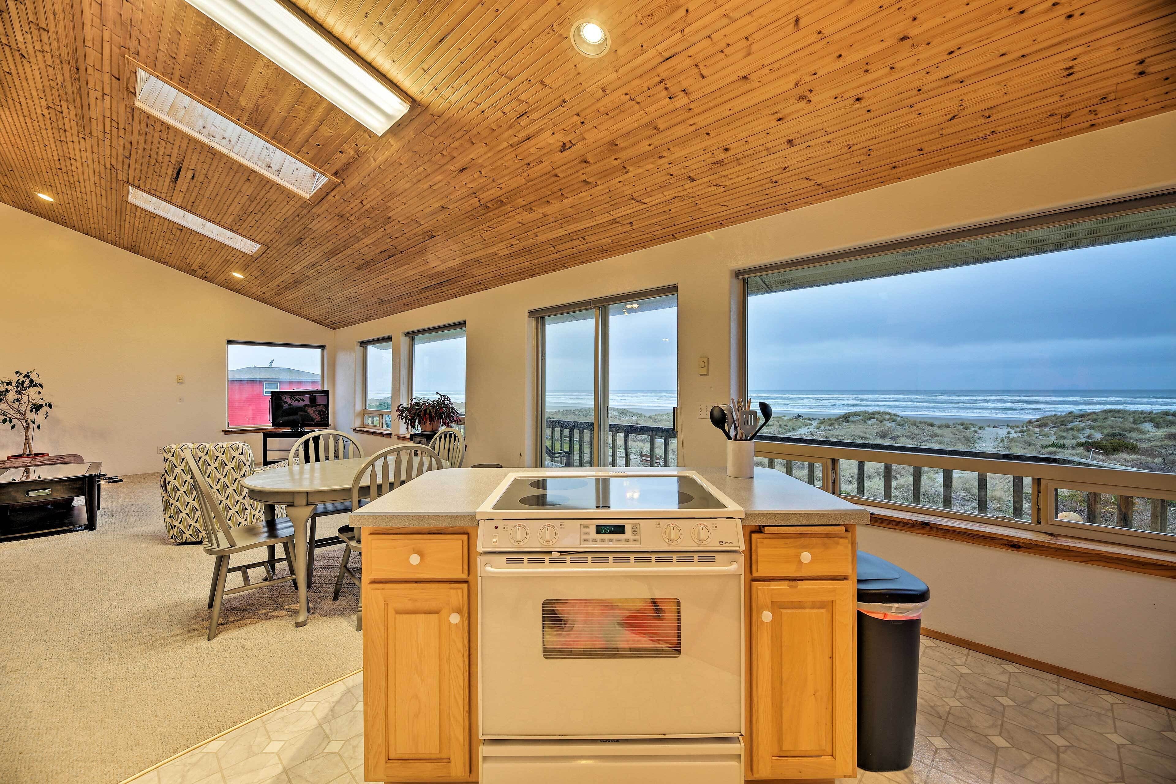 A kitchen with a large island, wooden ceiling, and a view of the beach.
