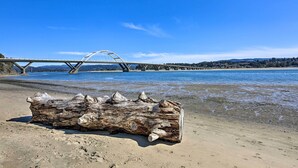 A log on a sandy beach with a bridge and hills in the background. - Sanderling Sea Cottages, Unit A: Pet Friendly! (Waldport)