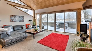 A modern living room with a black leather sofa, a wooden coffee table, and a red rug. Large windows offer a view of a snowy backyard. - 2 Mi to Park City Mtn: Townhome w/ Balcony (Park City)