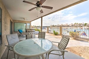 Eine überdachte Terrasse im Freien mit rundem Tisch und Stühlen, einem Grill und Blick auf einen Poolbereich.