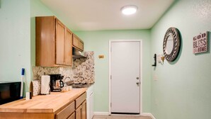 A kitchen with wooden cabinets, a countertop, a coffee maker, and a door with a mirror and a sign on the wall. - Soothing Studio w/ Lush Views: 2 Mi to Beach! (Smith River)