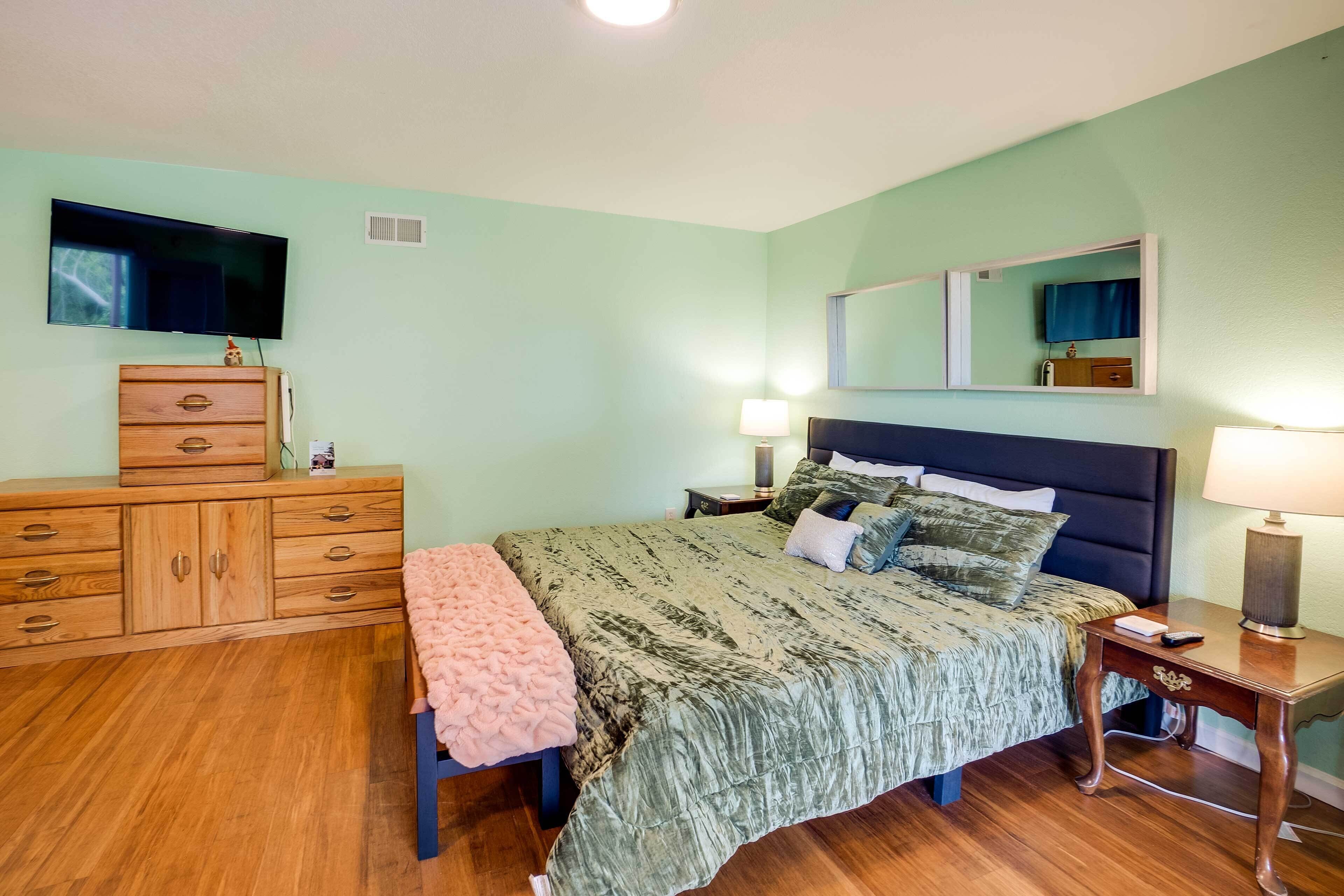 A bedroom with a bed, a dresser, a TV, and a bedside table with lamps.