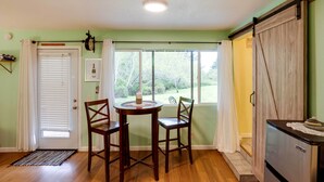 A room with a dining table and chairs, a refrigerator, a window with curtains, and a door with blinds. - Soothing Studio w/ Lush Views: 2 Mi to Beach! (Smith River)