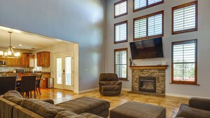 A spacious living room with a stone fireplace, a comfortable sofa set, and a kitchen area with wooden cabinets and a dining table. - Great Salt Lake House: 5,000 Sq Ft, Mtn Views! (Kaysville)