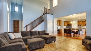 A spacious living room with a large sectional sofa, a wooden staircase, and a view into the kitchen area. - Great Salt Lake House: 5,000 Sq Ft, Mtn Views! (Kaysville)