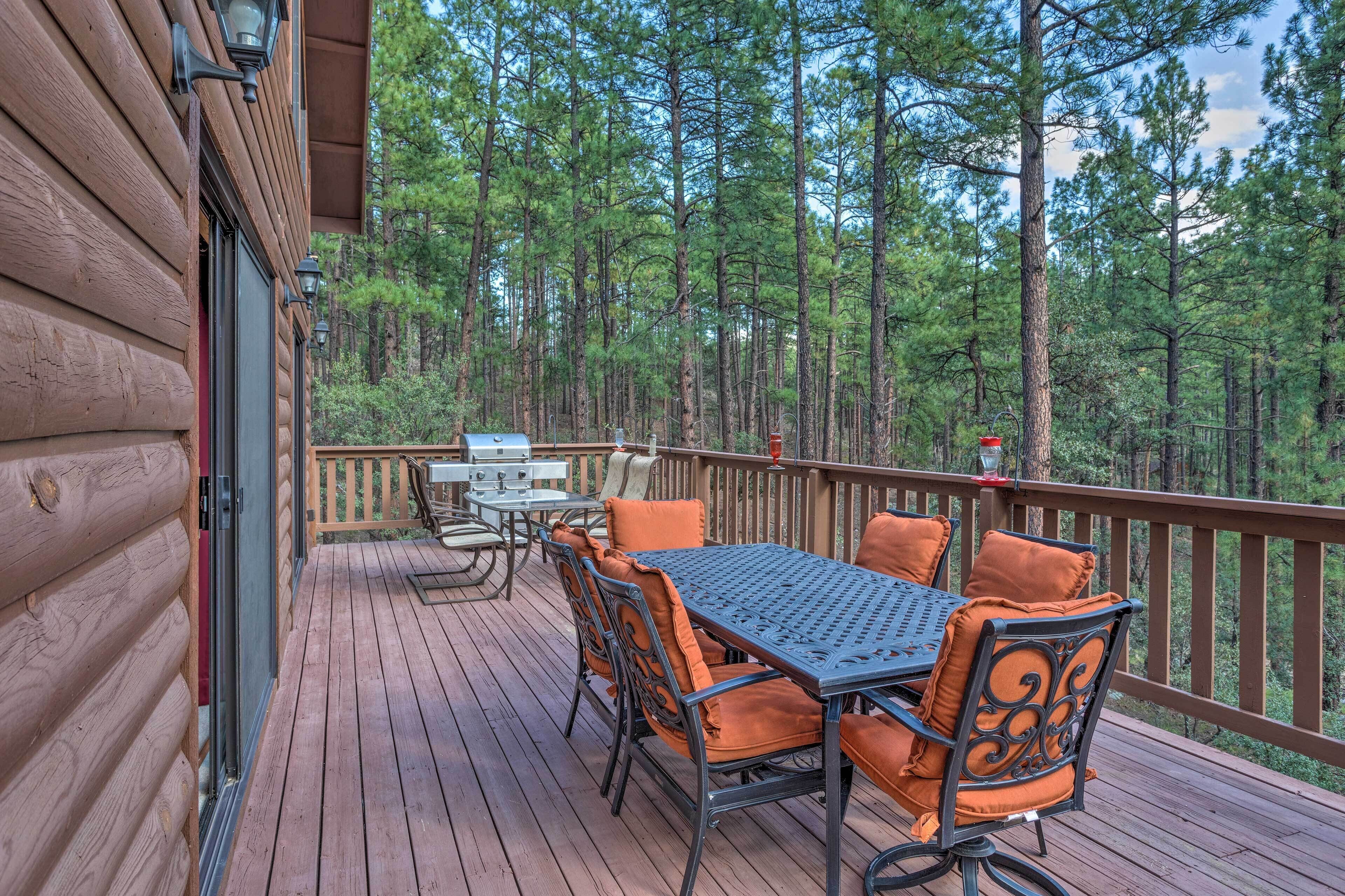 A wooden deck with a table and chairs, surrounded by a forest.