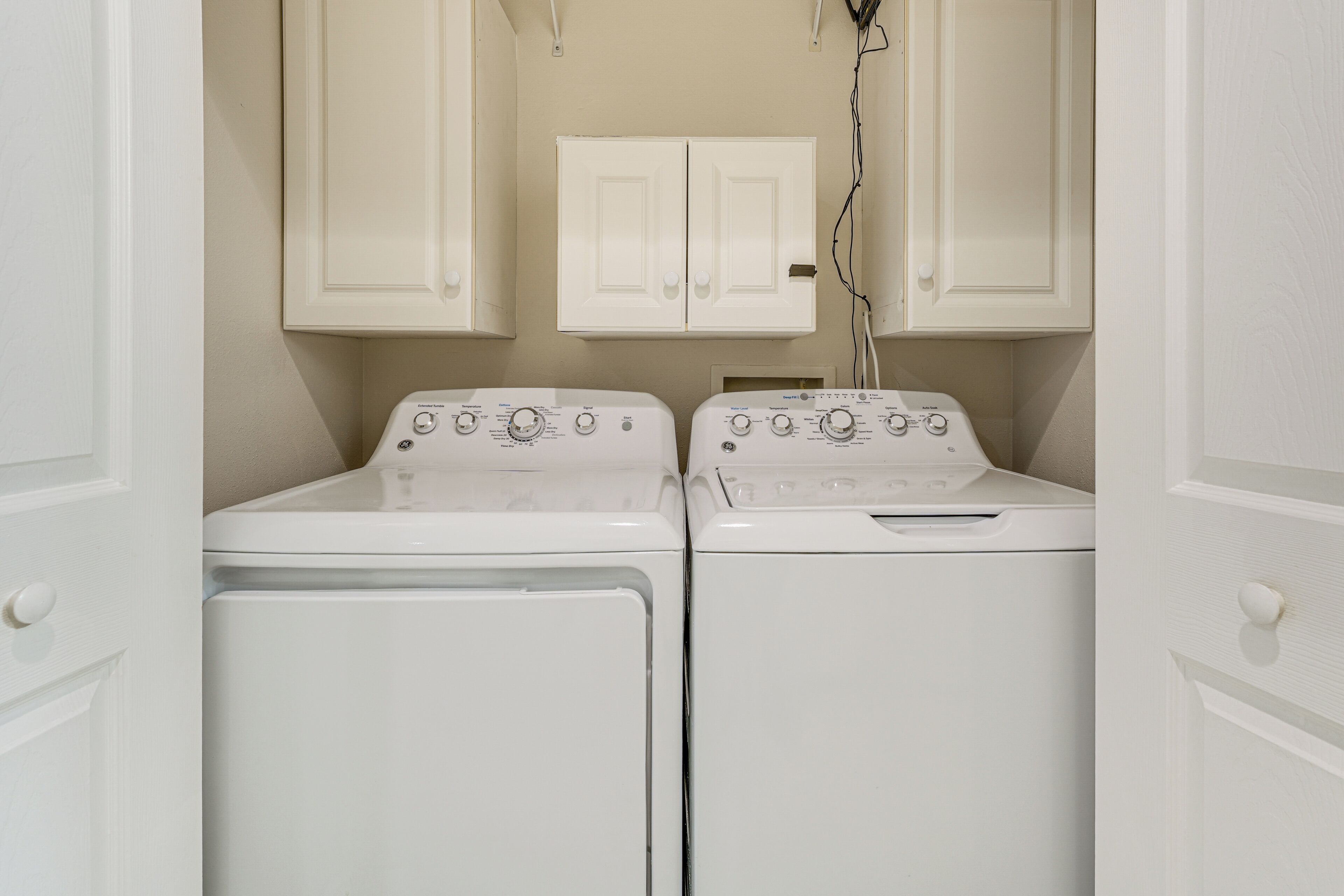 A laundry room with two white front-loading washing machines and a cabinet above them.