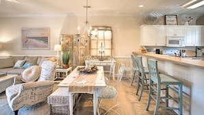 A dining area with a long table, chairs, and a chandelier. There is a kitchen area with cabinets and a microwave. - Little River Condo w/ Pool < 6 Mi to Beach! (Little River)
