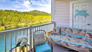 A balcony with a view of a lake and forest, a bed with a beach-themed bedspread, and a door with a turtle decoration. - Little River Condo w/ Pool < 6 Mi to Beach! (Little River)