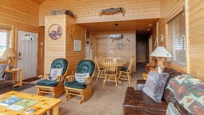 A cozy log cabin interior with a dining area, two rocking chairs, a leather sofa, and a fireplace. - Cozy Henrys Lake Escape - 20 Miles to Yellowstone! (Island Park)