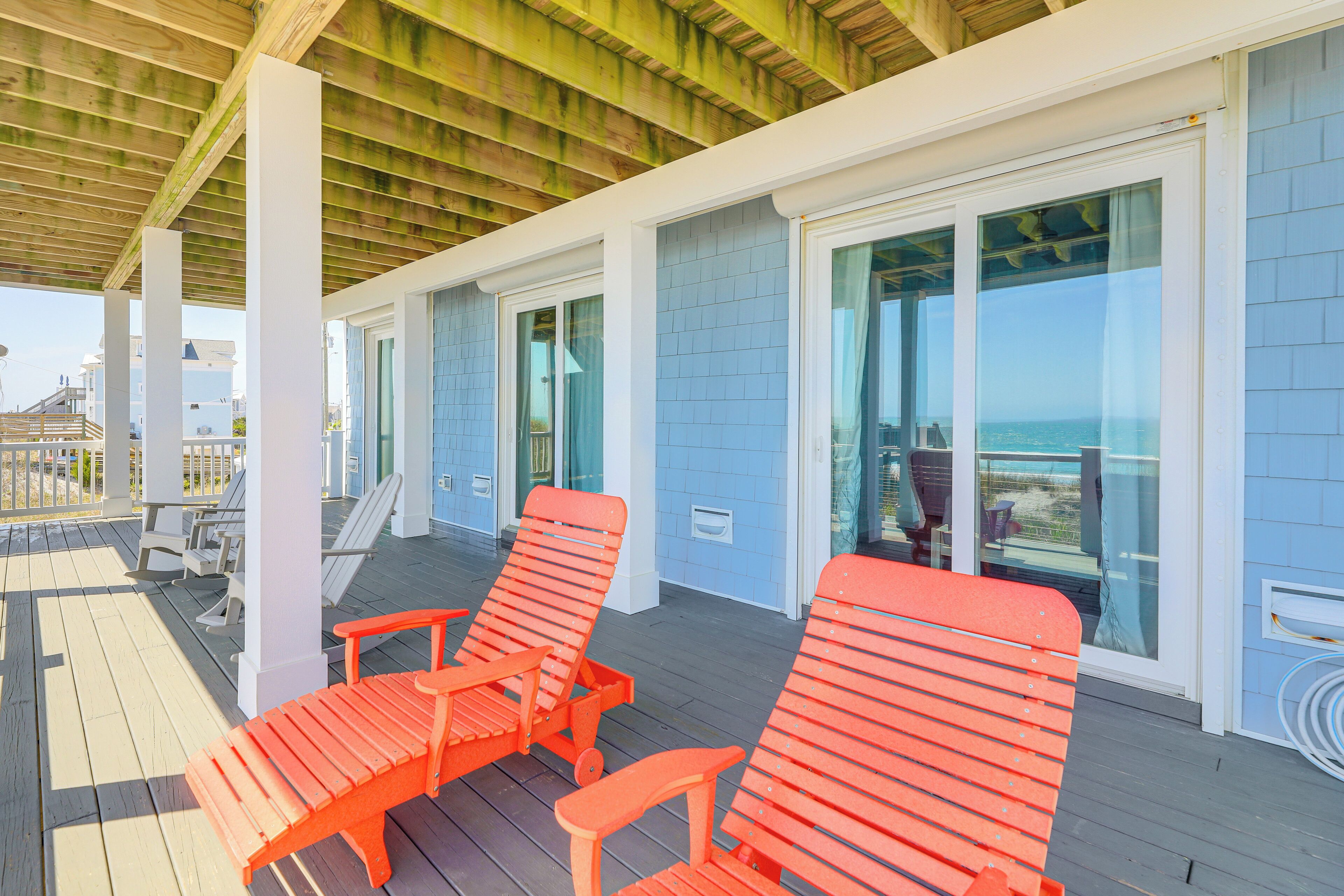 A covered outdoor area with wooden deck, white columns, and orange lounge chairs.