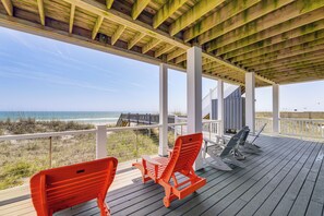 A covered deck with wooden railings, two orange Adirondack chairs, and a view of the beach and ocean.
