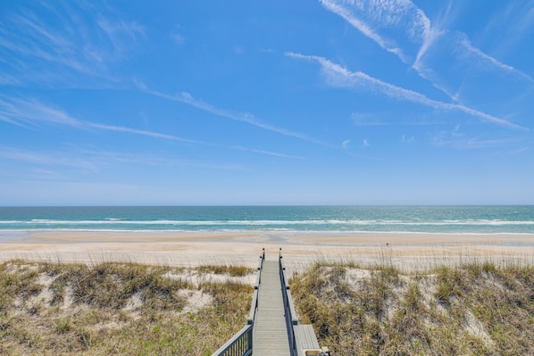 A wooden boardwalk leading to a beach with sand dunes and ocean views.