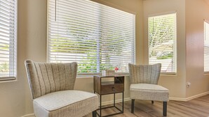 A room with two upholstered chairs, a small wooden side table, and a window with blinds. - Private Pool & Patio: Home in Surprise! (Surprise)
