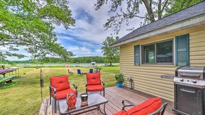 A deck with red outdoor furniture, a grill, and a view of a lake. - Cottage on Tubbs Lake w/ Fire Pit Near Skiing! (Mecosta)